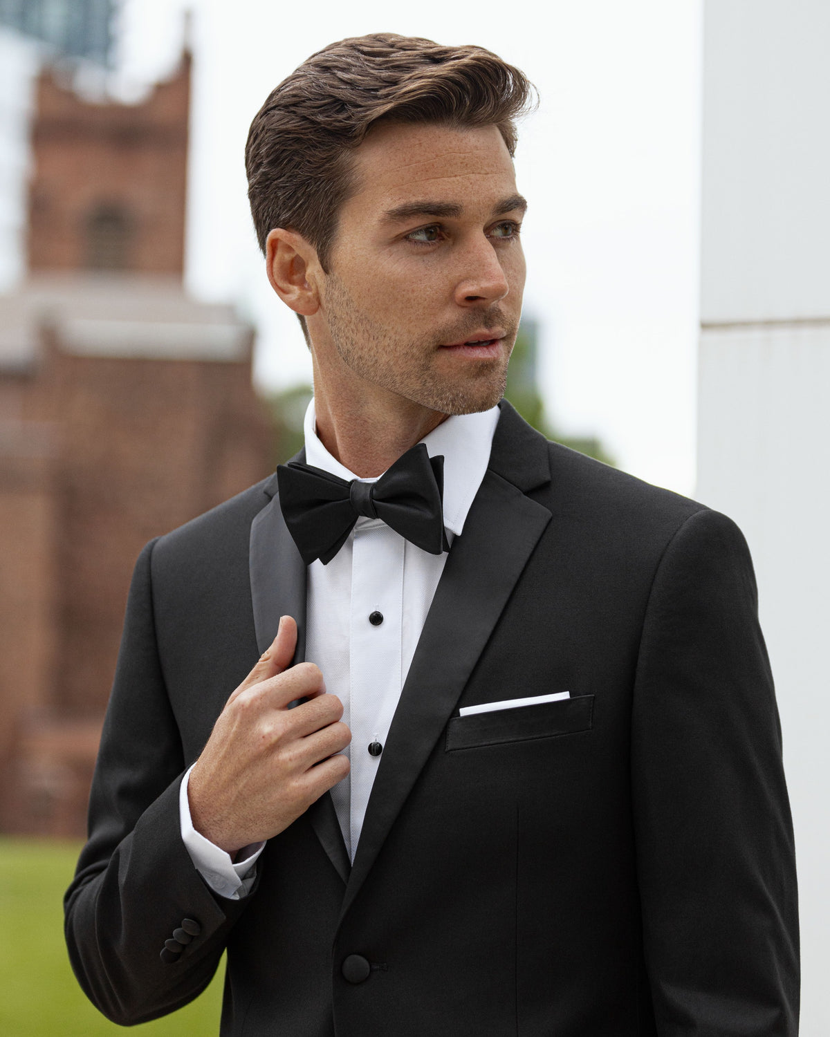 A man in a black tuxedo and bow tie adjusting his cuff