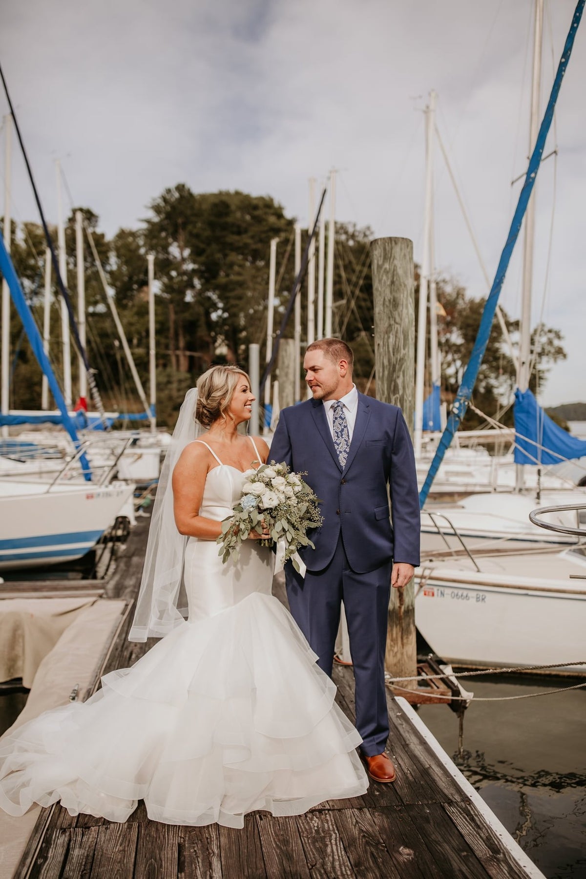 A groom in a navy suit with his bride on a marina dock