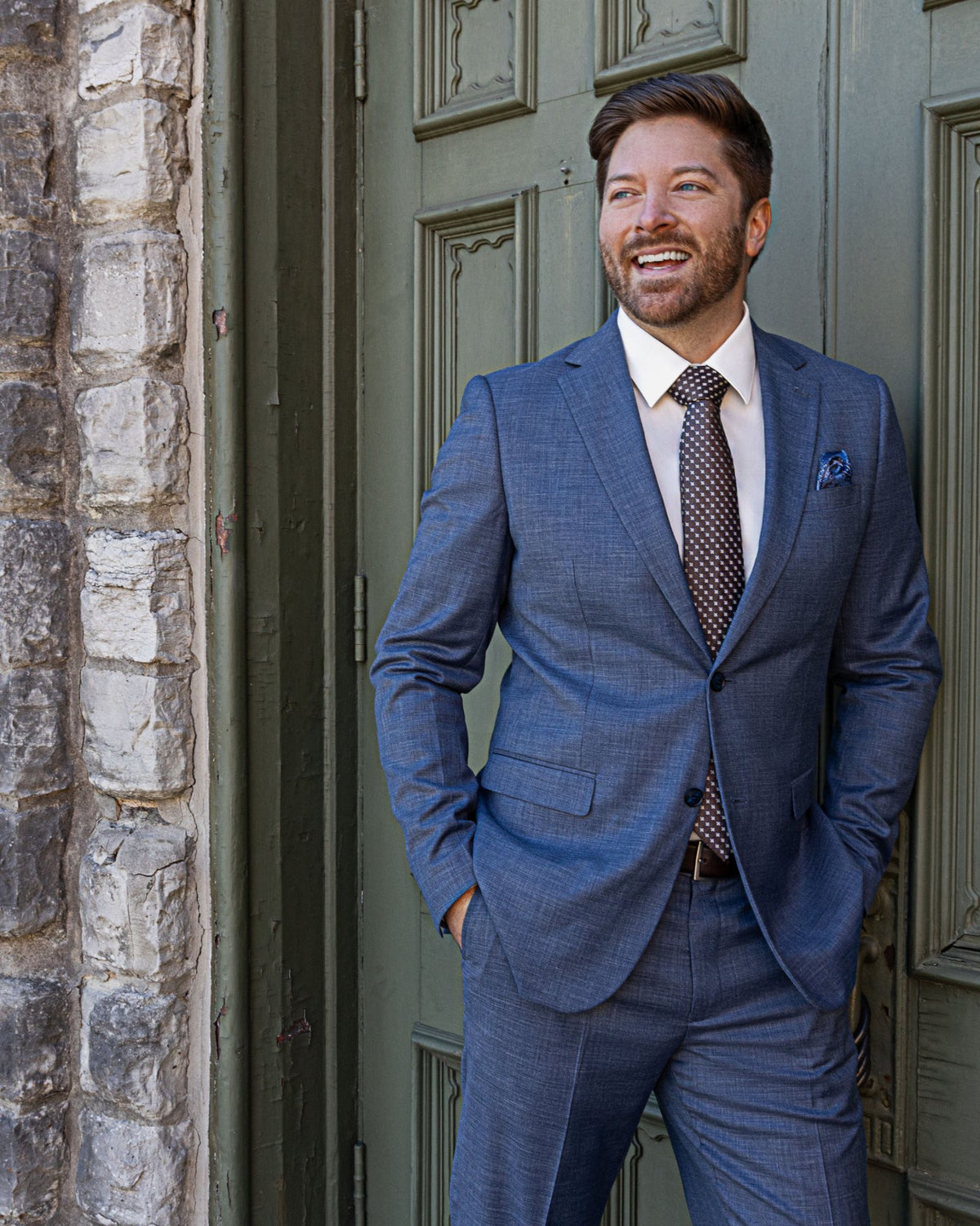 A smiling man in a blue Sterling Sewn suit and patterned tie at a green door in Chattanooga