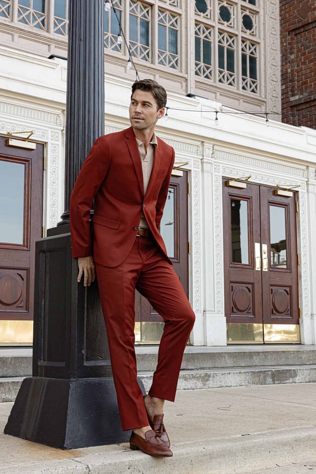 A man in a burgundy suit leaning on a lamppost outside a historic building