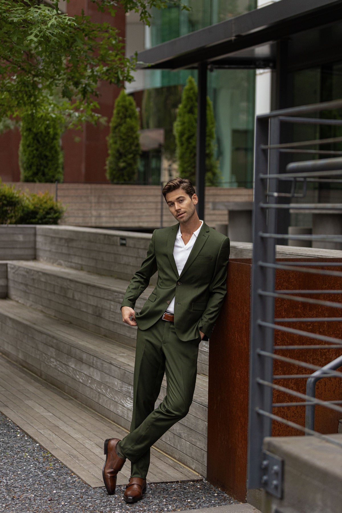 A man in an olive green suit leaning on a railing beside stone steps