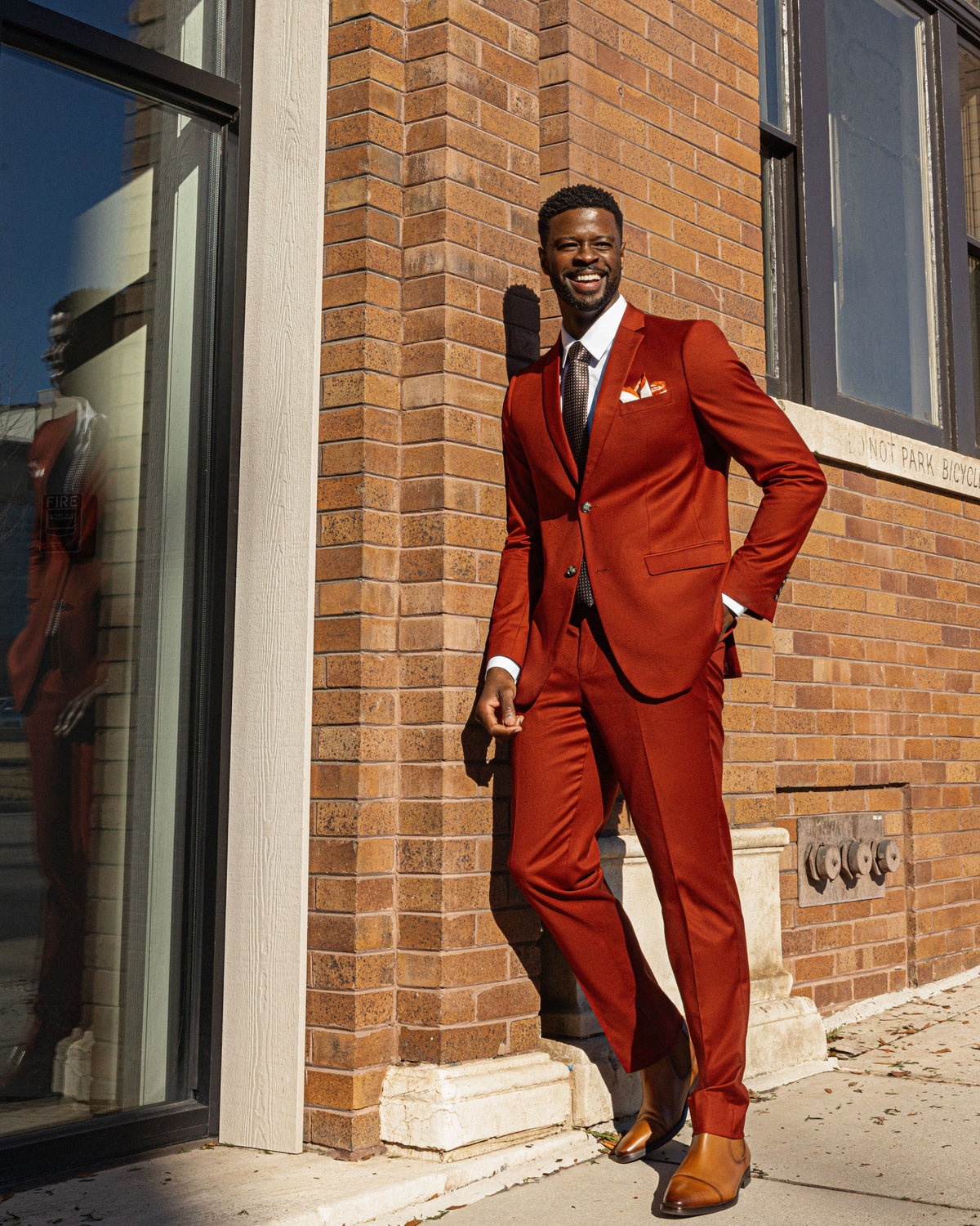 A man in a rust Sterling Sewn suit smiling against a brick storefront in downtown Chattanooga