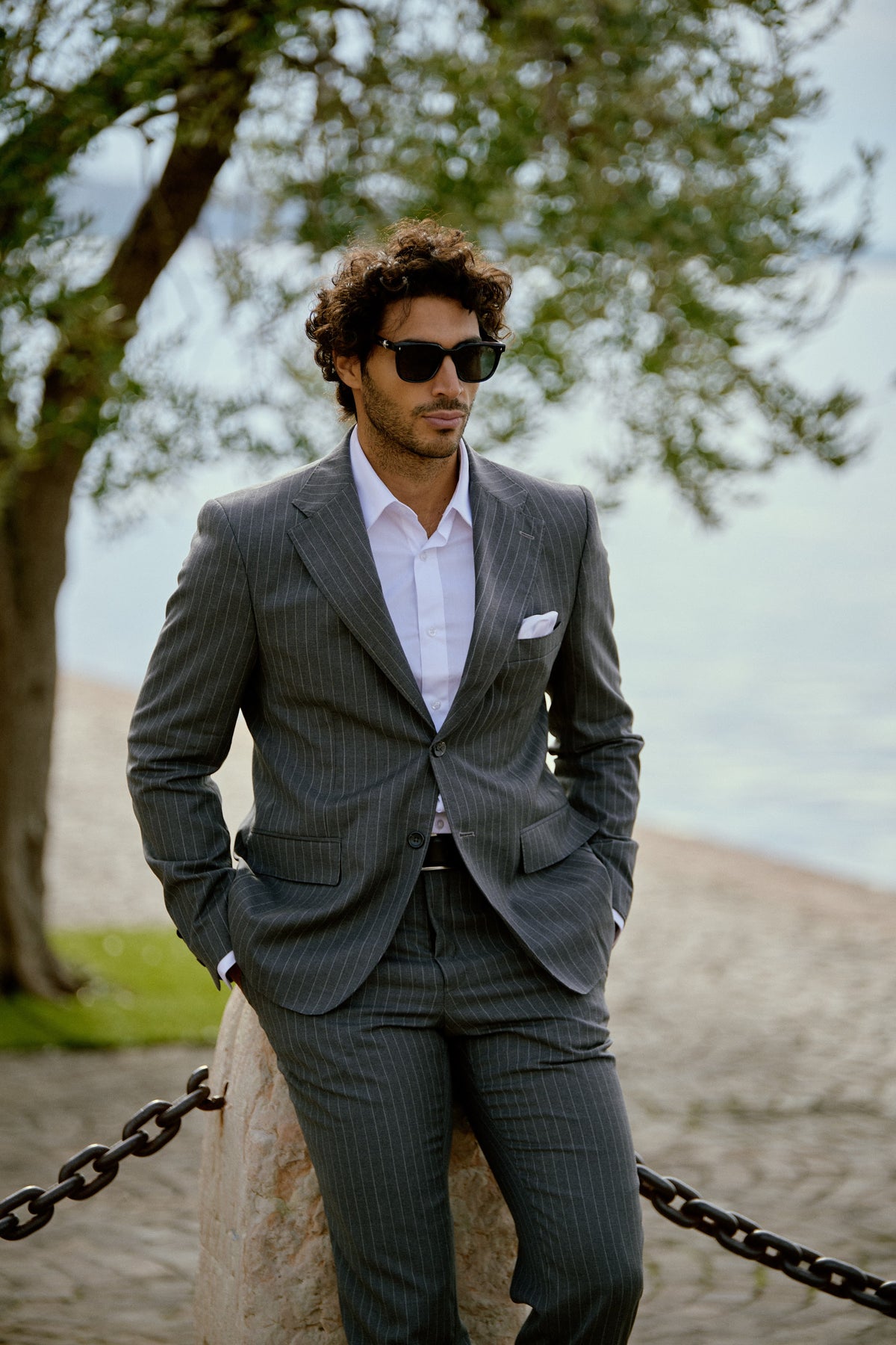A man in a charcoal check suit and sunglasses by the lake in Italy