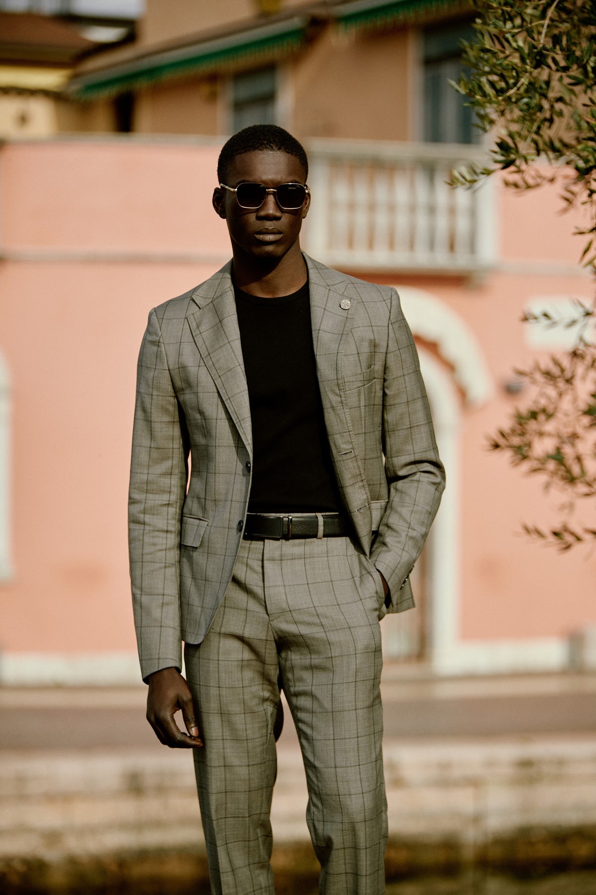 A man in a check suit and black tee against a pink wall in Italy
