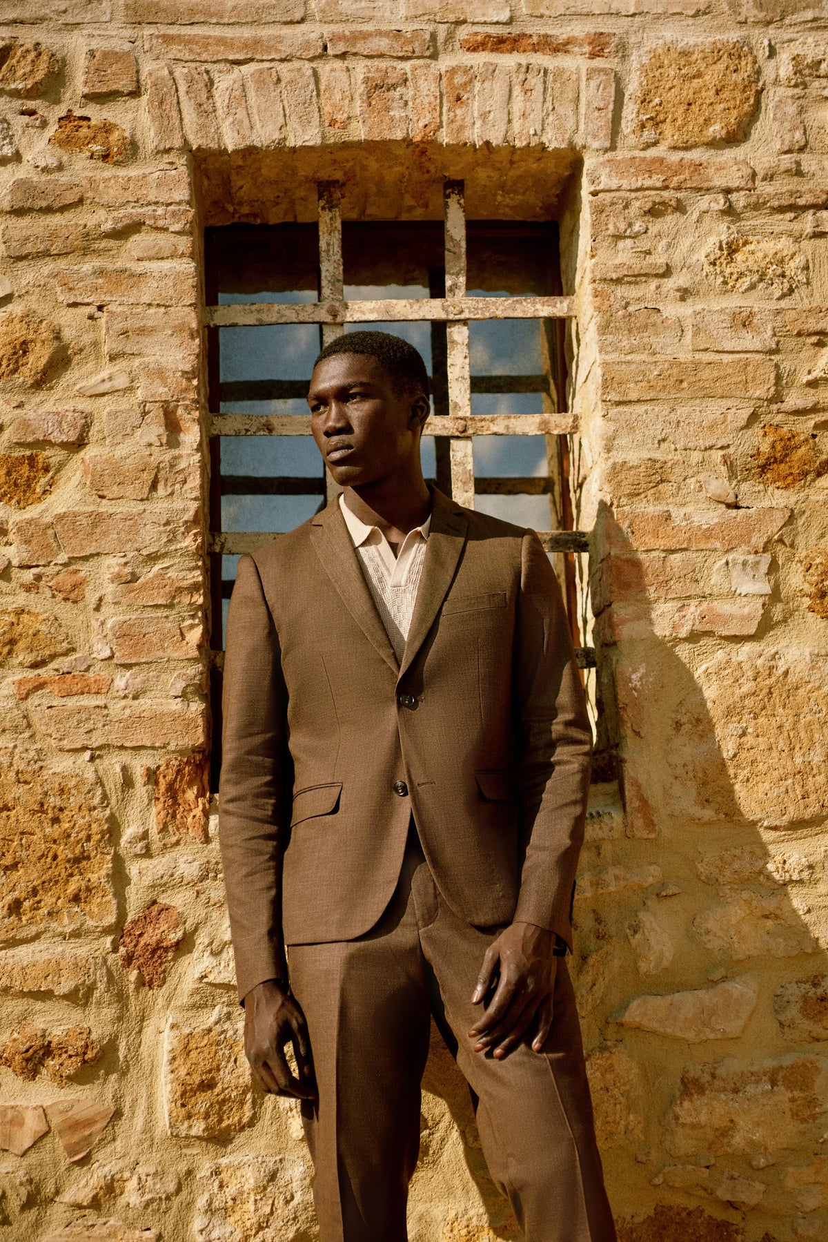 A man in a chocolate brown suit against a stone wall in Tuscany