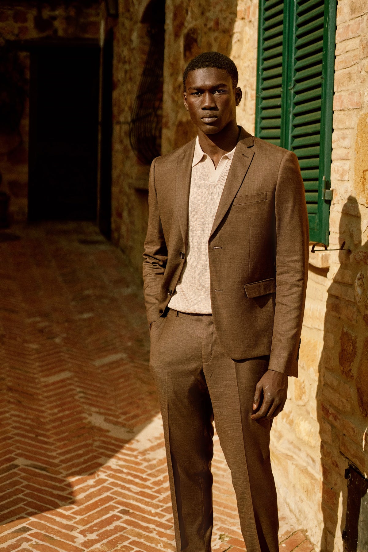 A man in a chocolate brown suit by green shutters in Tuscany
