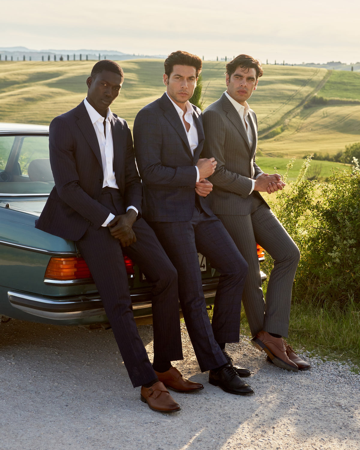 Three men in dark suits with a vintage car in Tuscany