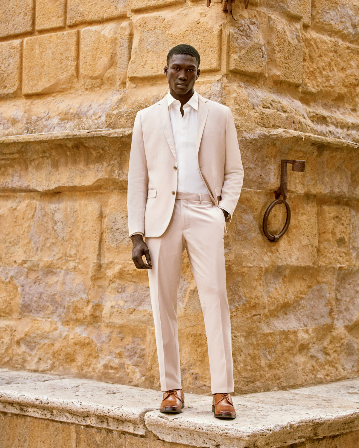 A man in an ivory summer suit against a stone wall in Tuscany