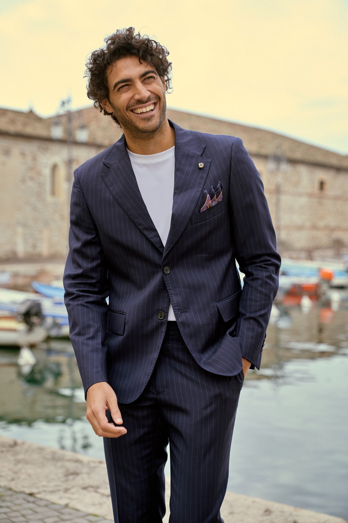 A smiling man in a navy suit by the harbor in Lazise, Italy