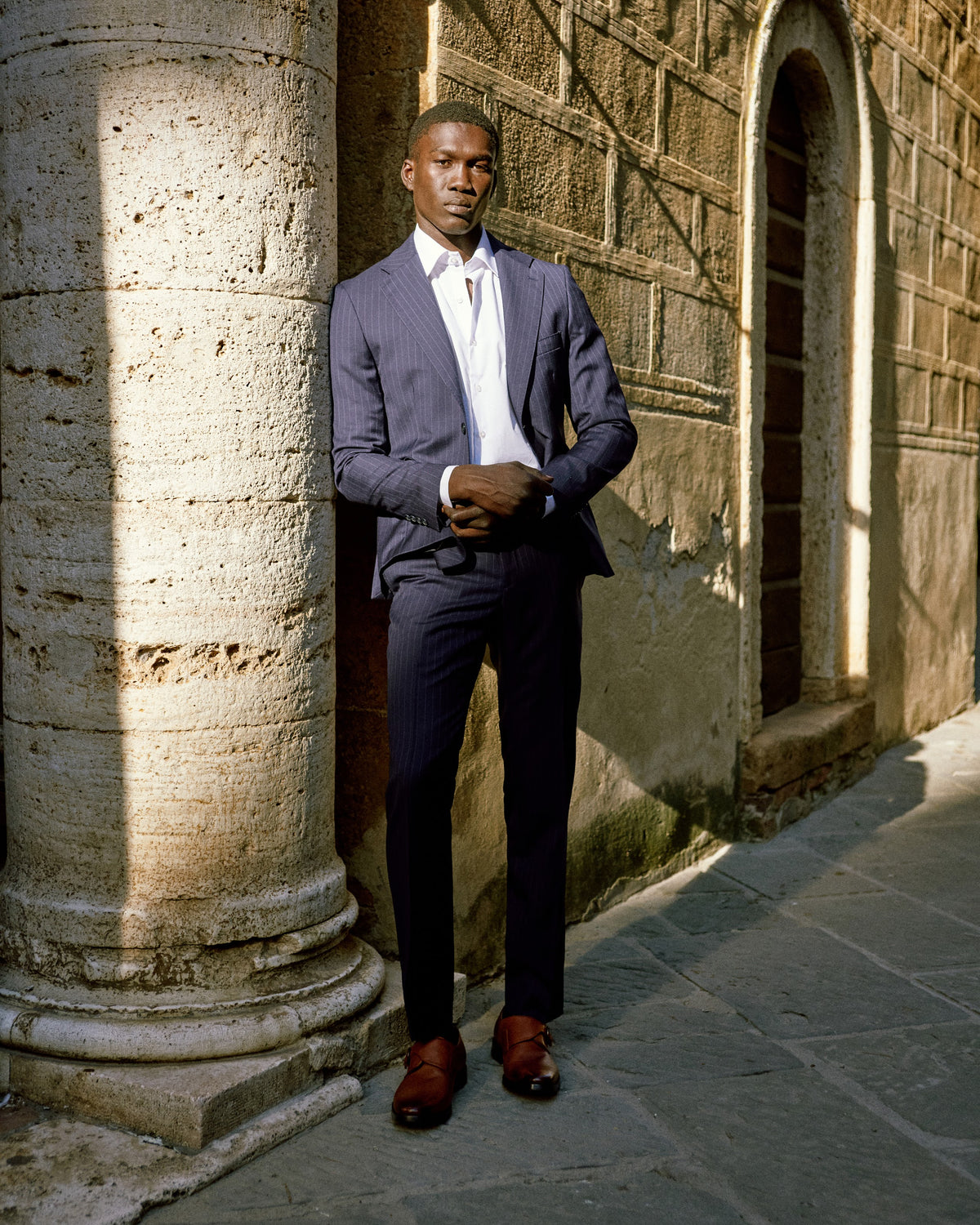 A man in a periwinkle blue suit between stone columns in Tuscany