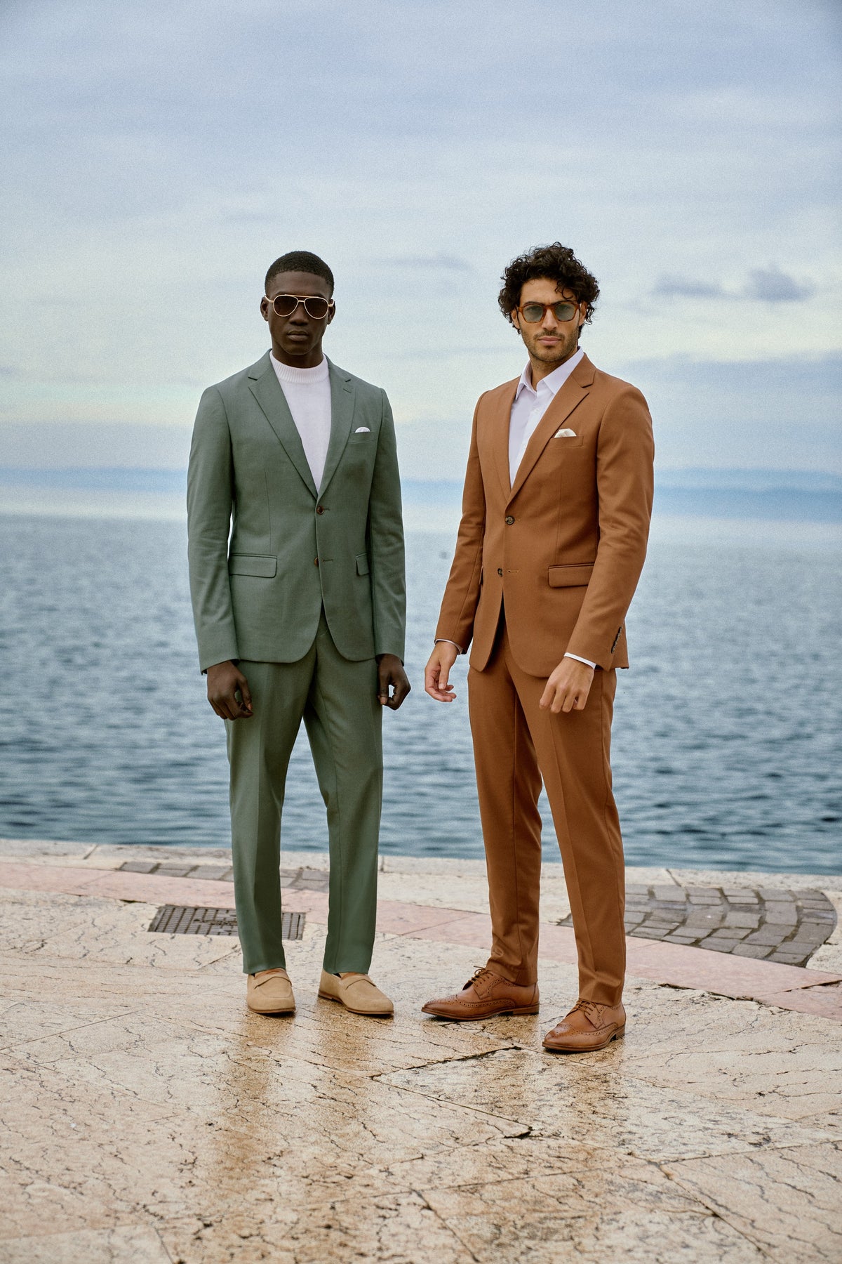 Two men in sage green and cognac suits on a pier at Lake Garda