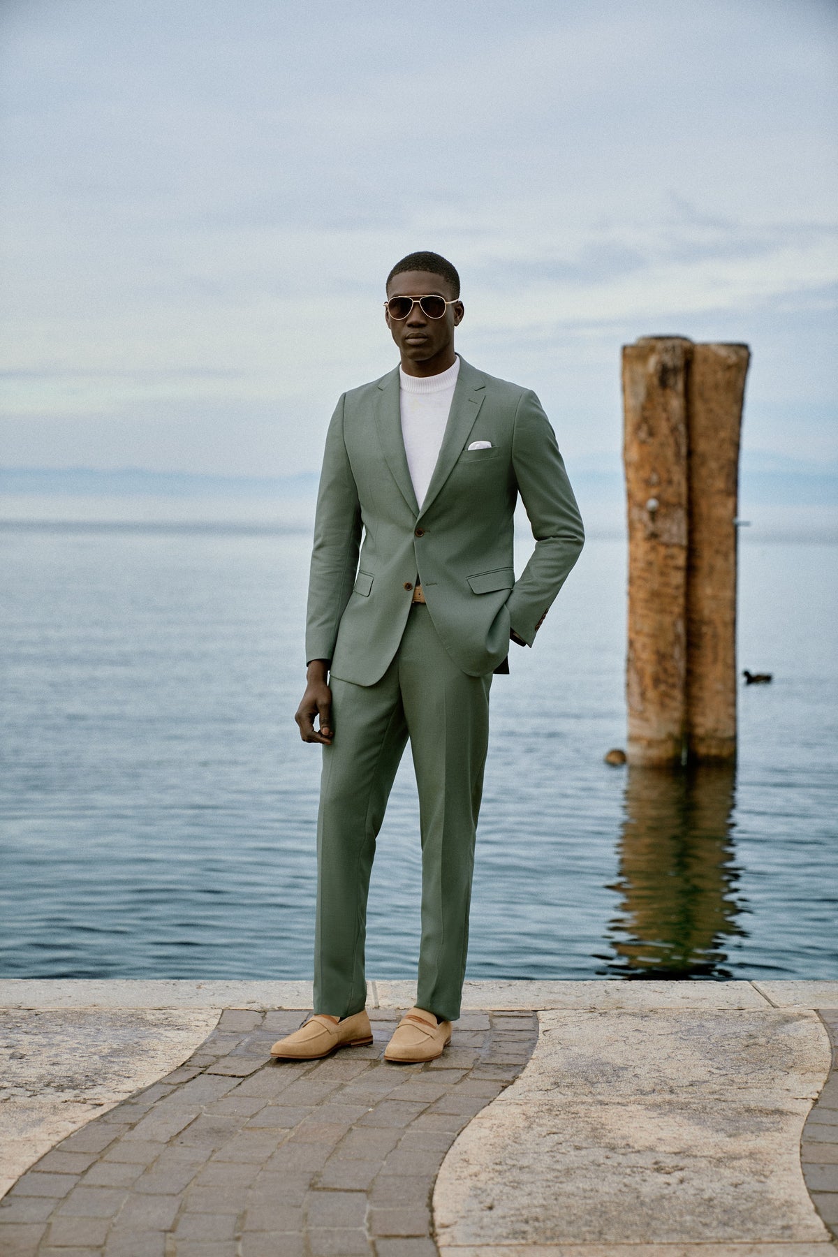 A man in a sage green suit on a lakeside pier in Italy