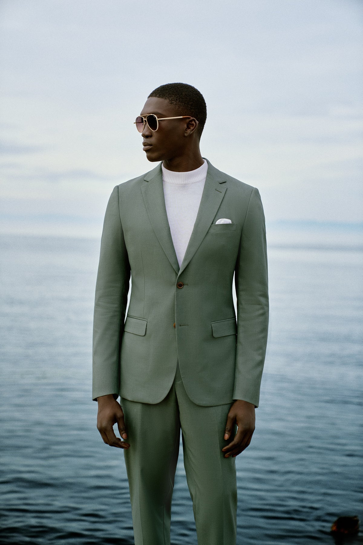 A man in a sage green suit and cream knit by Lake Garda, Italy