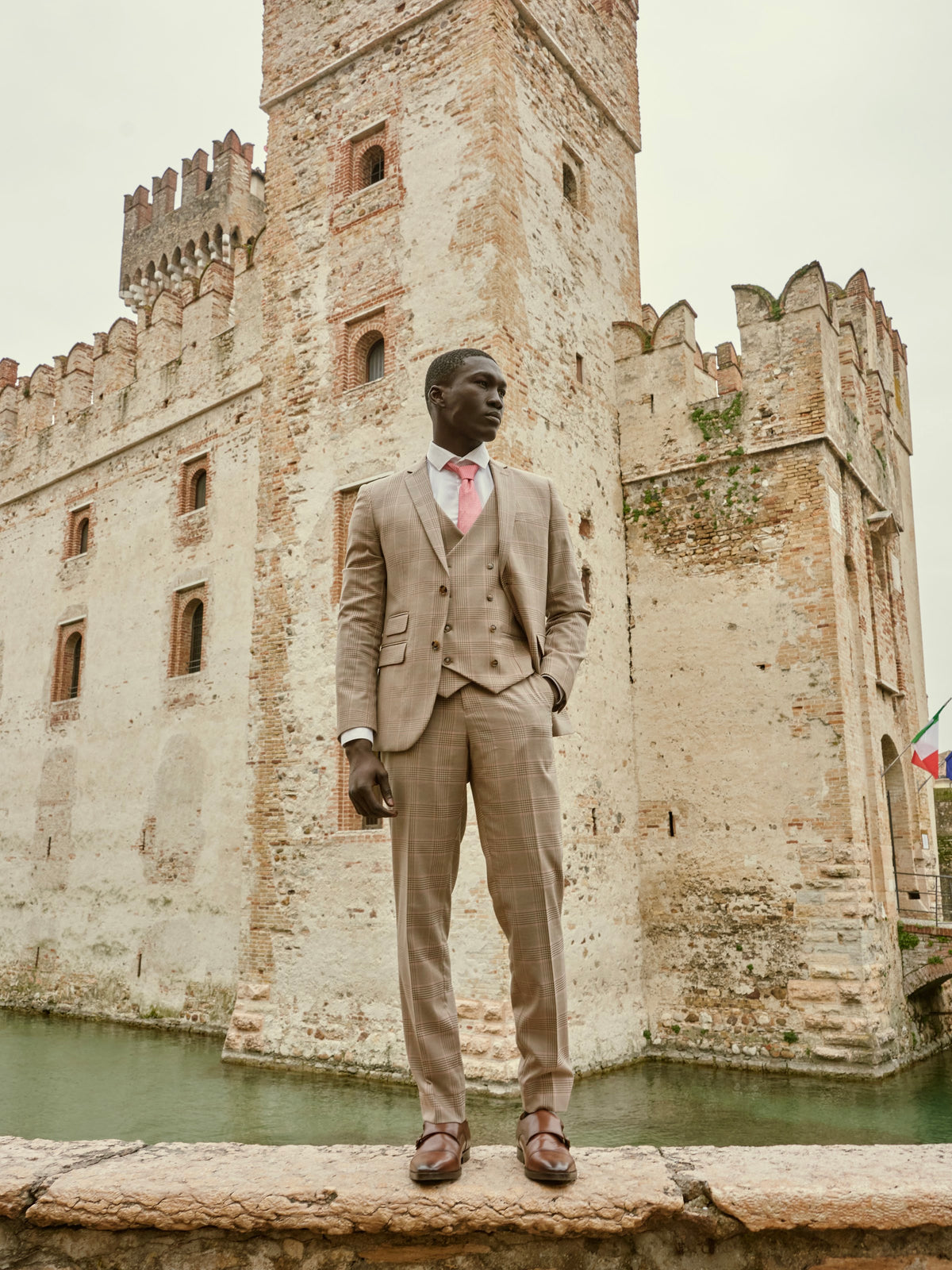 A man in a tan three-piece suit before the castle at Sirmione, Italy