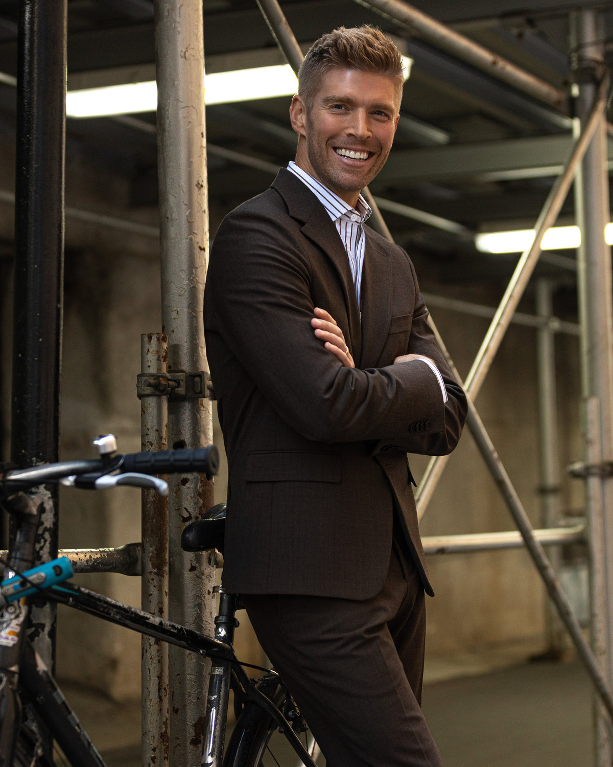 A smiling man in a dark brown suit with arms crossed