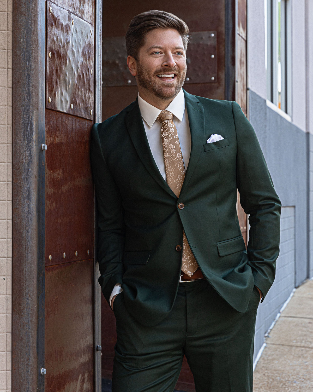 A smiling man in a forest green suit and gold tie
