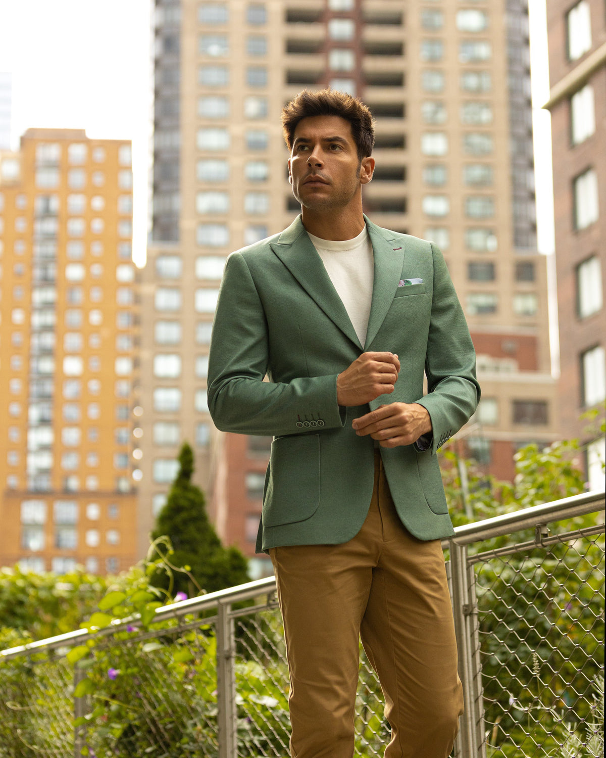 A man in a green sport coat, white tee and tan trousers