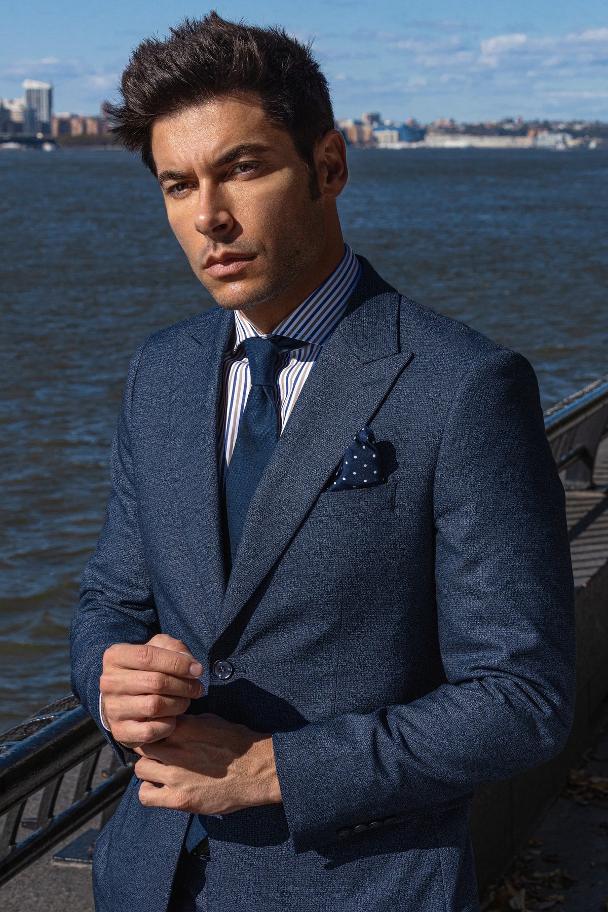 A man in a navy suit and patterned tie by the water