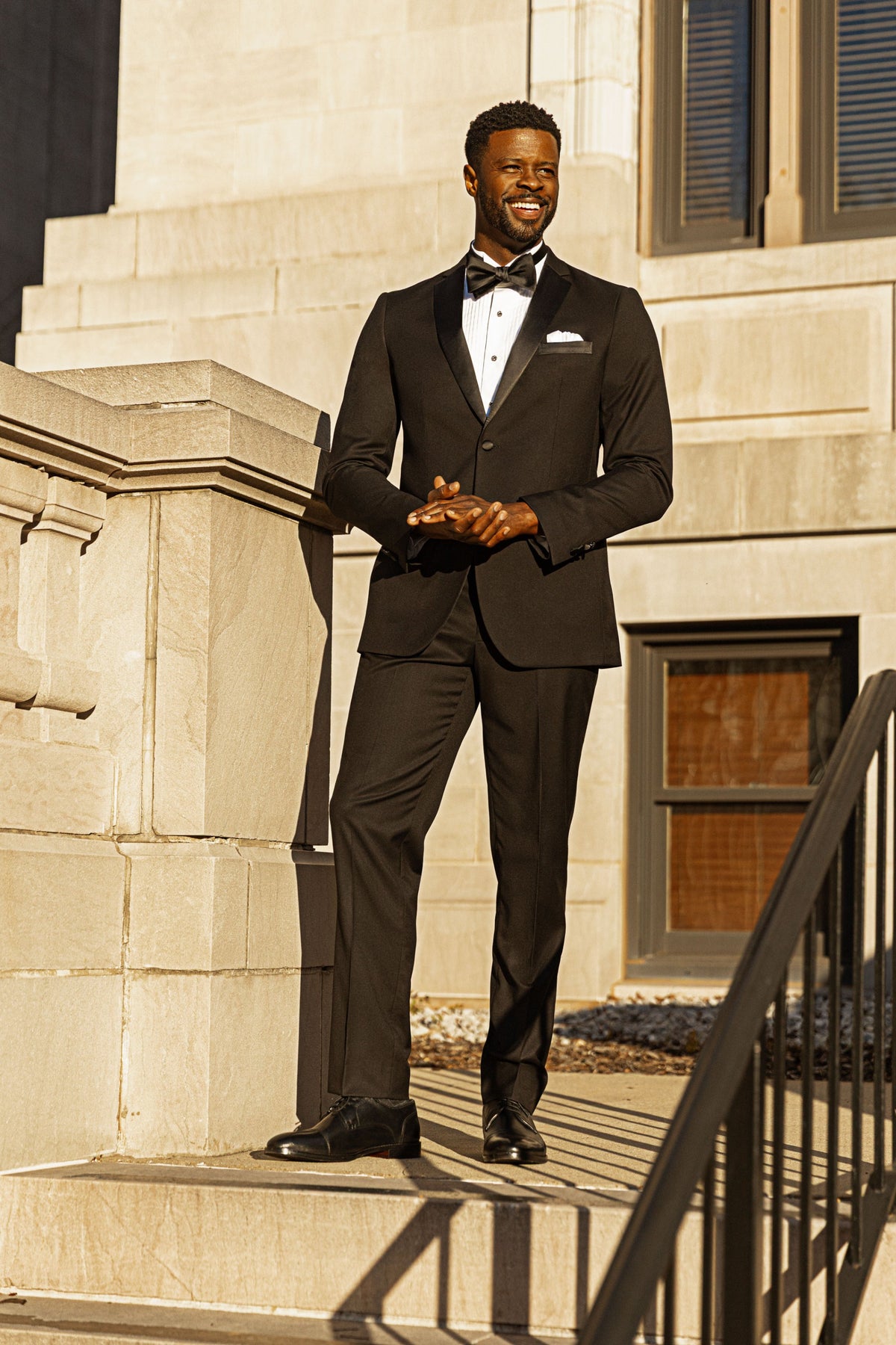 A man in a black tuxedo and bow tie on stone steps