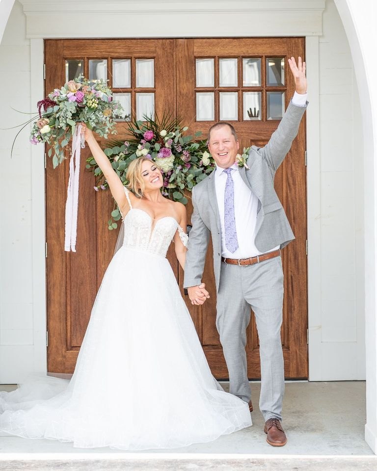 A groom in a light gray suit and his bride in front of chapel doors