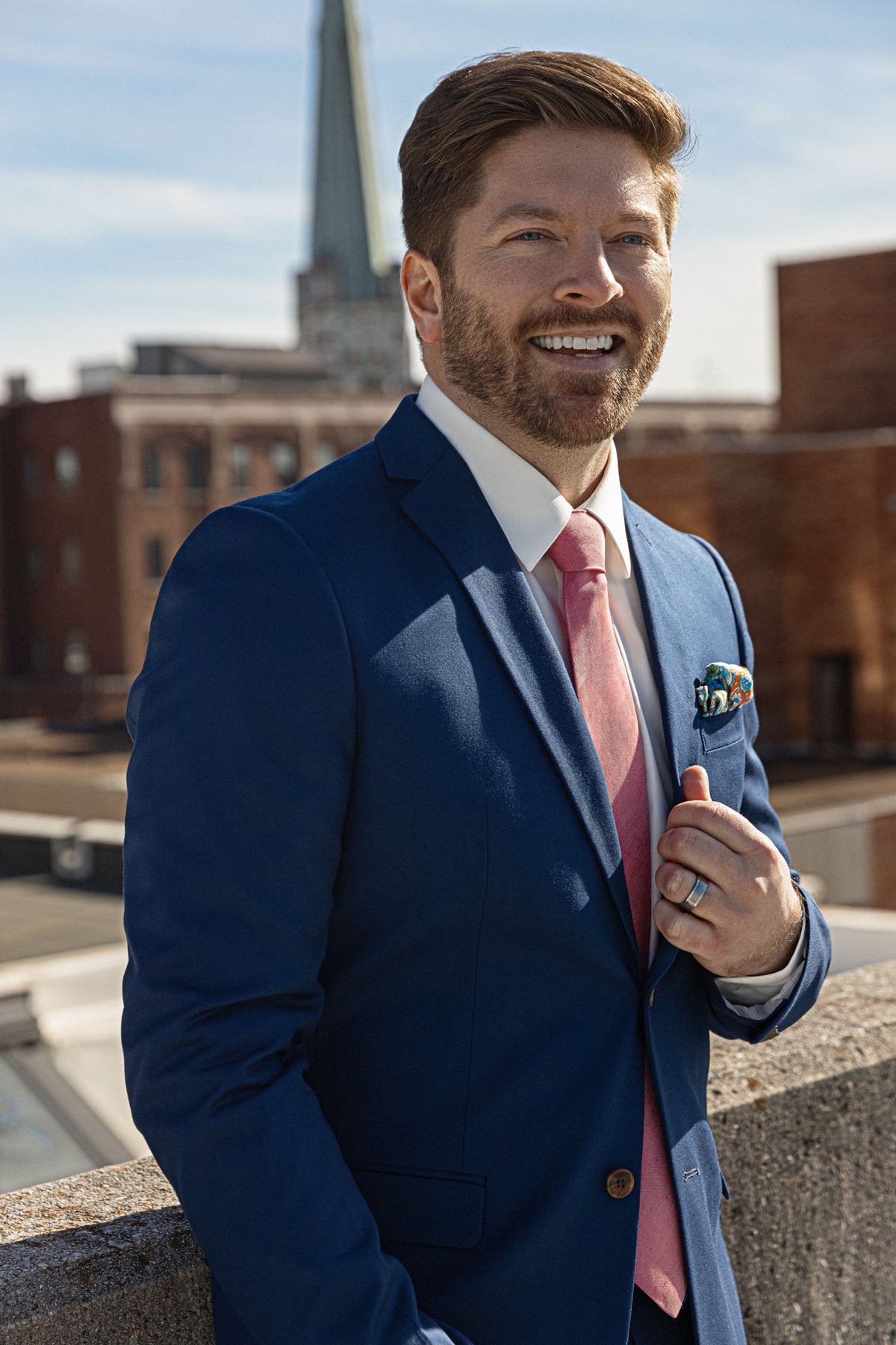 Groom in a navy Sterling Sewn suit with a blush tie, smiling outside in downtown Chattanooga